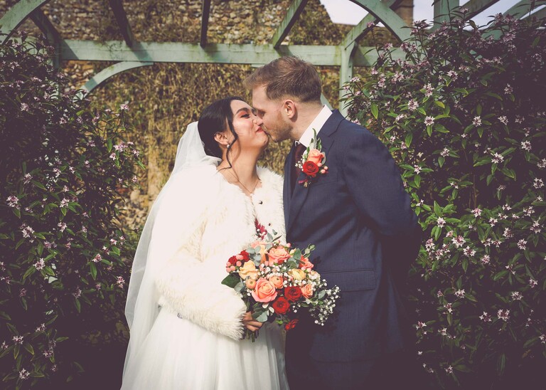 A bride and groom kissing at a winter wedding under a pergola painted green in abbey gardens in bury st edmunds on a wedding day photographed by suffolk wedding photographer Hayley Denston Photography