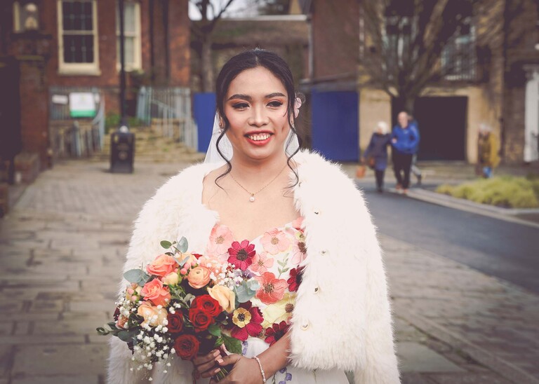 A bride stood with a fluffy white cardi in her colourful wedding dress with a bright wedding bouquet on a wedding day in bury st edmunds photographed by suffolk wedding photographer Hayley Denston Photography