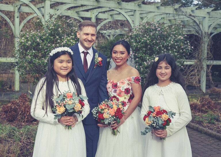 A formal group shot with a bride and groom and their flowergirls in Abbey Gardens in Bury St Edmunds on a wedding day photographed by Suffolk Wedding Photographer Hayley Denston Photography