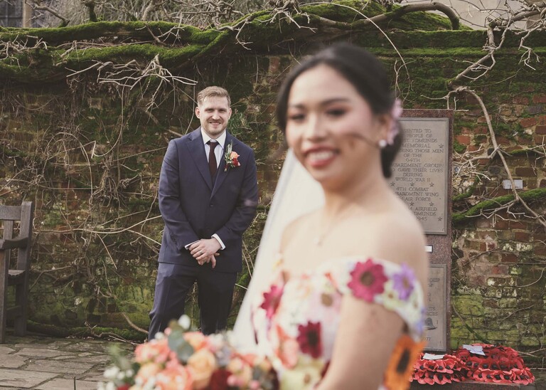A groom smiling at his bride in a walled garden on a winter wedding day in Abbey Gardens in Bury St Edmunds on a wedding day photographed by Suffolk Wedding Photographer Hayley Denston Photography