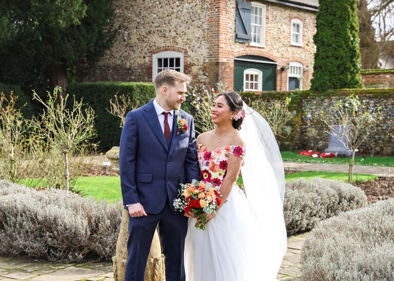 A bride and groom smiling at each other holding hands in a walled garden on a winter wedding day in Abbey Gardens in Bury St Edmunds on a wedding day photographed by Suffolk Wedding Photographer Hayley Denston Photography