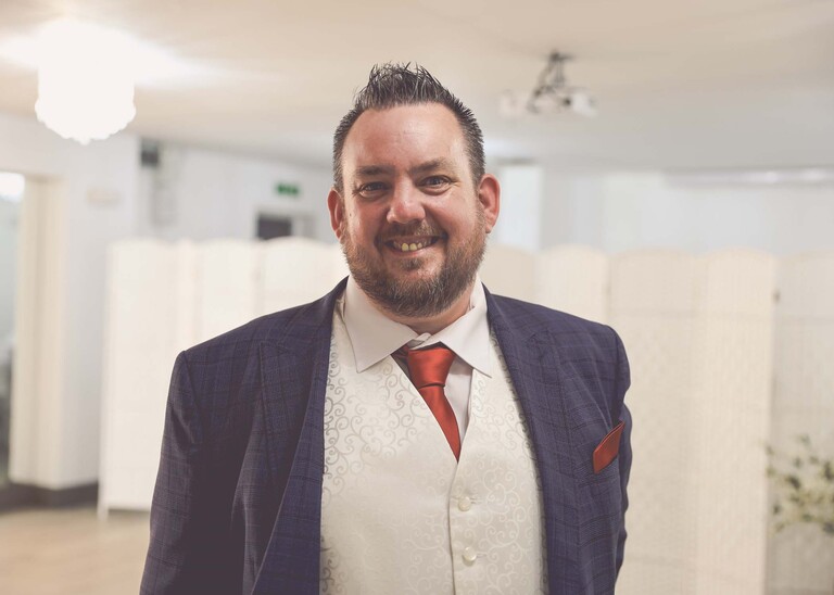 A groom smiling on his wedding day in a navy suit with a burnt orange tie on a wedding day at Venue 16 captured by suffolk wedding photographer Hayley Denston Photography