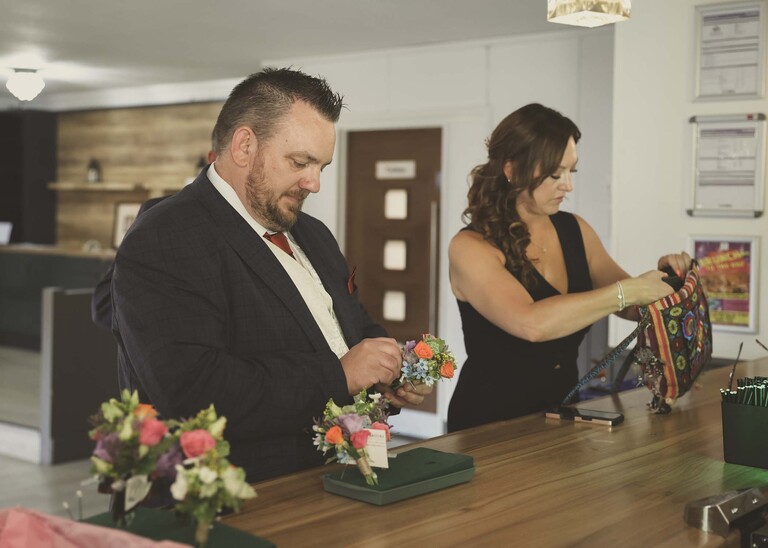 A groom and his bestwoman sorting buttonholes on a bar table top on a wedding day at Venue 16 captured by suffolk wedding photographer Hayley Denston Photography