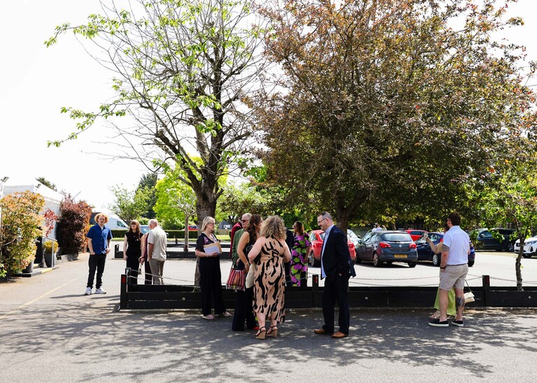 Guests mingling under trees in a car park to avoid the heat on a wedding day at Venue 16 captured by suffolk wedding photographer Hayley Denston Photography