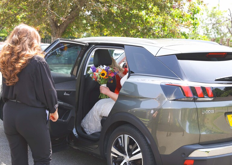 A bride and her bright floral bouquet getting out of a car on a wedding day at Venue 16 captured by suffolk wedding photographer Hayley Denston Photography
