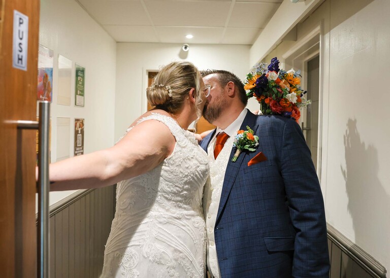 A bride and groom having a kiss in a venue corridor after their wedding ceremony on a wedding day at Venue 16 captured by suffolk wedding photographer Hayley Denston Photography