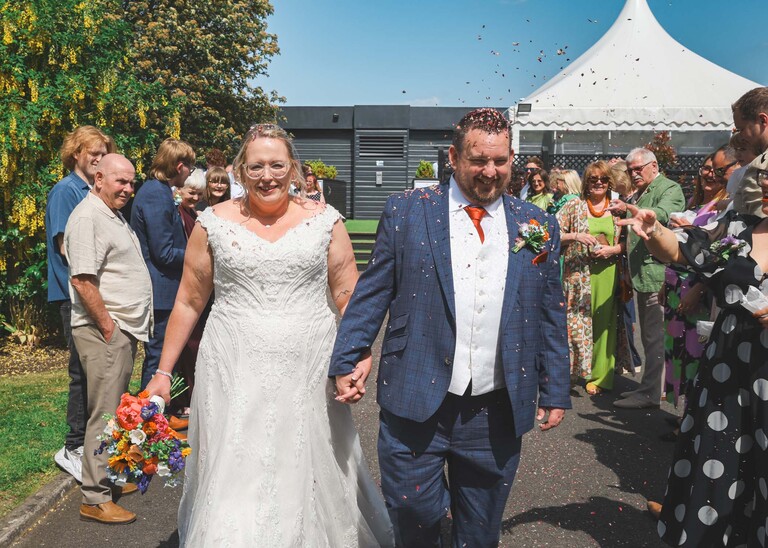 A bride and groom being showered in confetti on a blue sky day on a wedding day at Venue 16 captured by suffolk wedding photographer Hayley Denston Photography