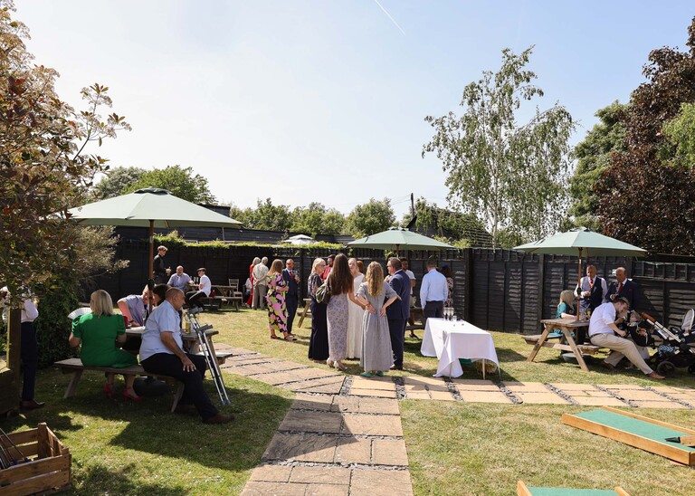 Guests mingling and being under garden parasols at a wedding reception on a wedding day at Venue 16 captured by suffolk wedding photographer Hayley Denston Photography