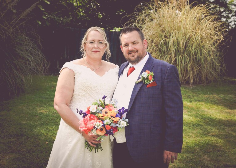 A bride and groom with pampus grass behind them and bright floral bouquet on a wedding day at Venue 16 captured by suffolk wedding photographer Hayley Denston Photography