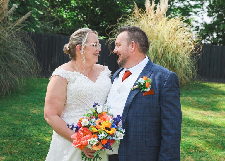 A bride and groom looking at each other with bright florals on a wedding day at Venue 16 captured by suffolk wedding photographer Hayley Denston Photography