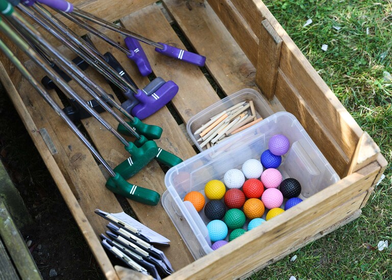 Bright golf balls and clubs and score cards and pencils in a wooden crate on a wedding day at Venue 16 captured by suffolk wedding photographer Hayley Denston Photography