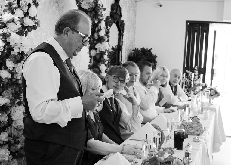 A father of the bride giving a speech on a wedding day in black and white with the top table watching on a wedding day at Venue 16 captured by suffolk wedding photographer Hayley Denston Photography