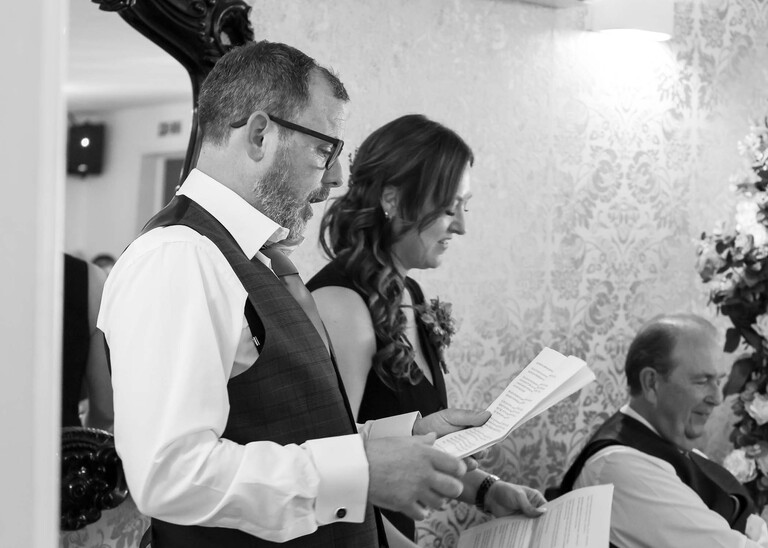 A black and white photo of a bestman and bestwoman giving wedding speeches on a wedding day at Venue 16 captured by suffolk wedding photographer Hayley Denston Photography