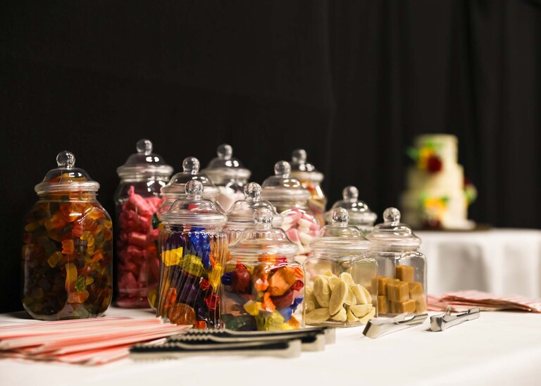 Sweet jars full with sweets and the wedding cake in the background on a wedding day at Venue 16 captured by suffolk wedding photographer Hayley Denston Photography