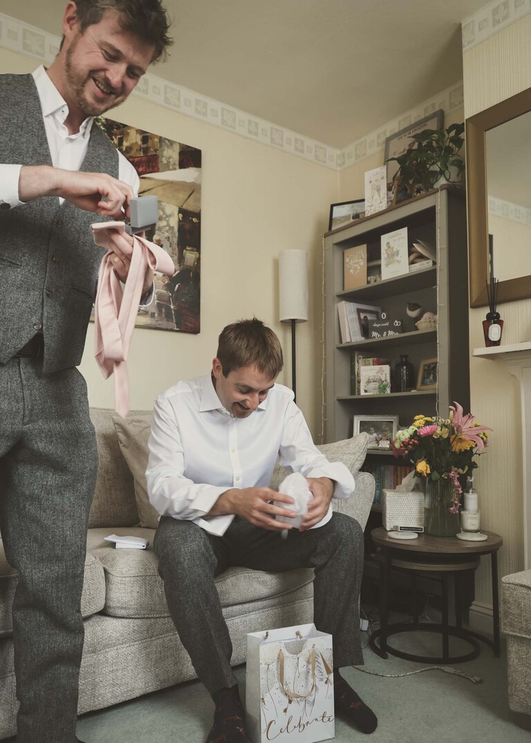 A groom sat down opening gifts from his bride on a wedding day at Haughley Park Barn photographed by suffolk wedding photographer Hayley Denston Photography