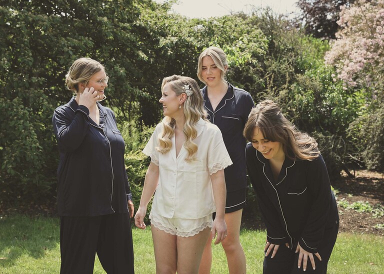 A bride laughing with her bridesmaids in a garden all in their pjs on a wedding day at Haughley Park Barn photographed by suffolk wedding photographer Hayley Denston Photography