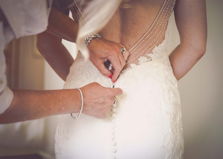 A close up of hands doing up buttons on a brides wedding dress on a wedding day at Haughley Park Barn photographed by suffolk wedding photographer Hayley Denston Photography