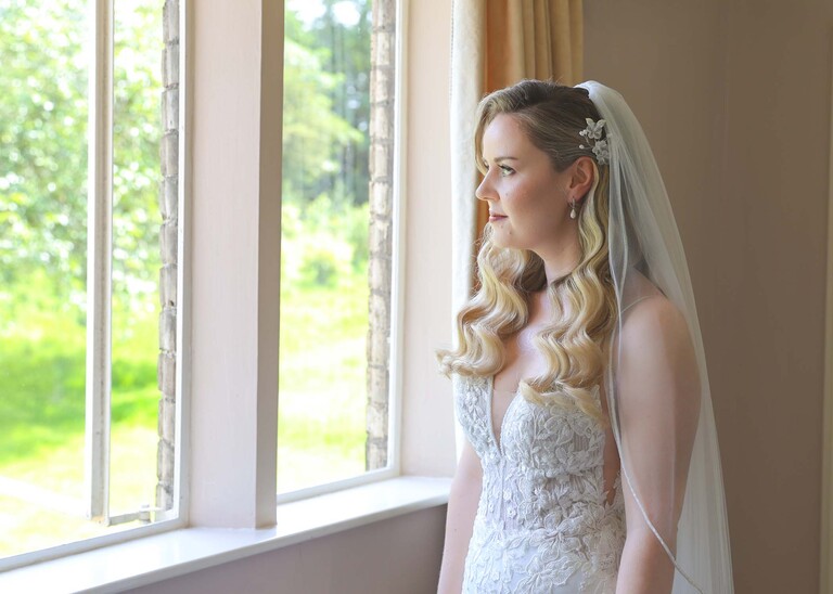 A bride looking wistfully out of a window before she goes for her wedding ceremony on a wedding day at Haughley Park Barn photographed by suffolk wedding photographer Hayley Denston Photography
