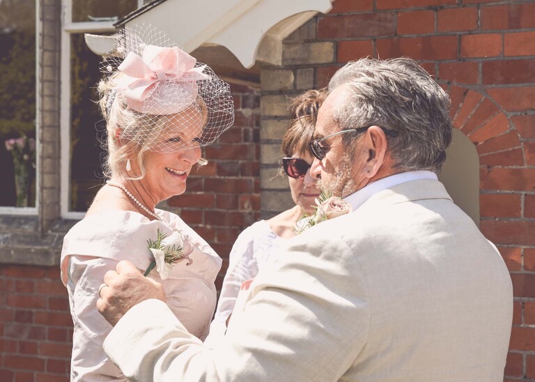 A father of the bride helping his wife with her corsage on a wedding day at Haughley Park Barn photographed by suffolk wedding photographer Hayley Denston Photography