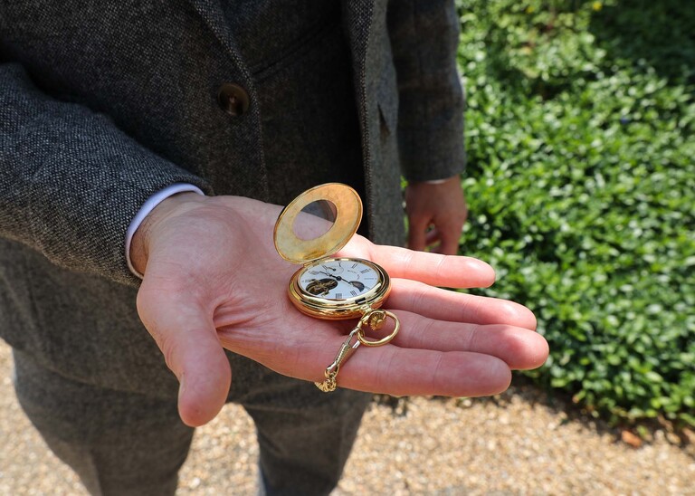 A gold pocket watch held open on the grooms hand on a wedding day at Haughley Park Barn photographed by suffolk wedding photographer Hayley Denston Photography