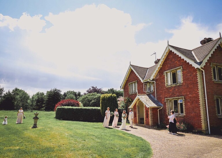 A farmhouse with the bride and bridesmaids walking across to their wedding venue on a wedding day at Haughley Park Barn photographed by suffolk wedding photographer Hayley Denston Photography