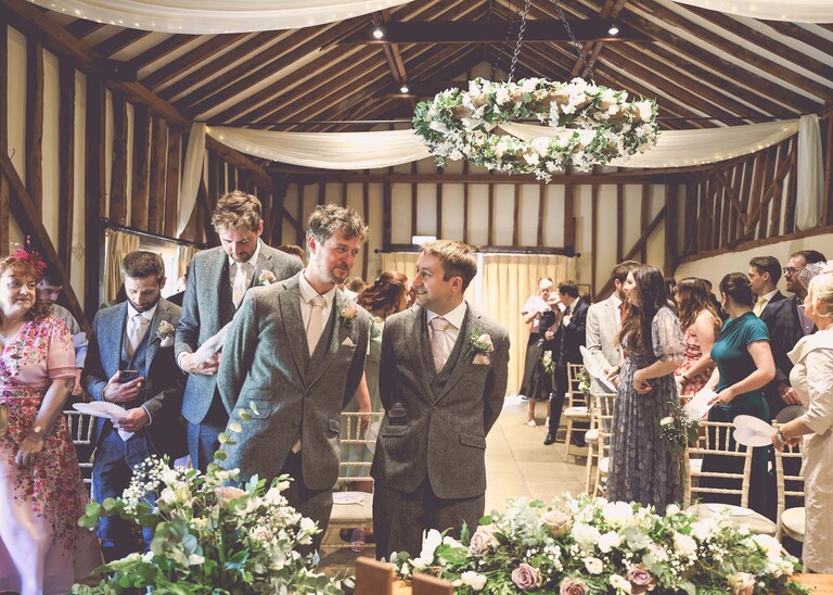 A groom and his bestman talking and waiting at the front of the ceremony room for the brides arrival on a wedding day at Haughley Park Barn photographed by suffolk wedding photographer Hayley Denston Photography