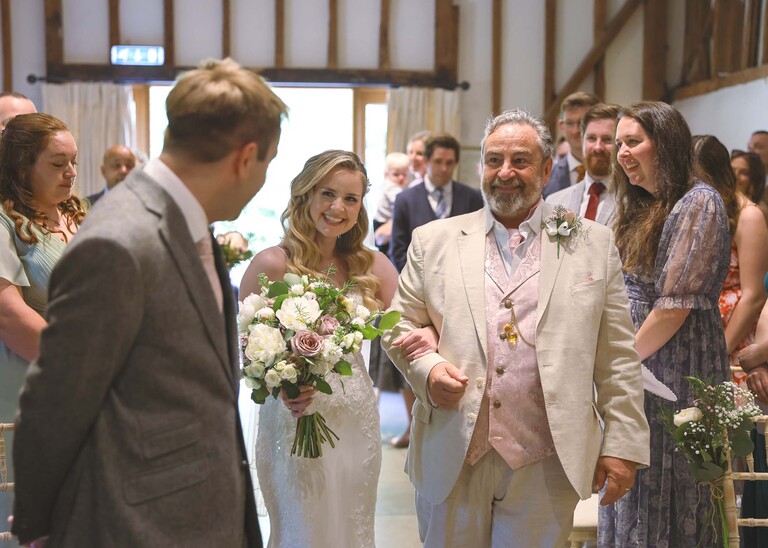 A father of the bride and bride approaching the groom as they walk down the aisle on a wedding day at Haughley Park Barn photographed by suffolk wedding photographer Hayley Denston Photography