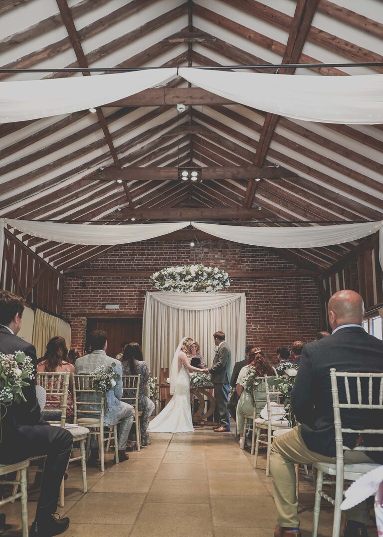 A bride and groom in their barn wedding ceremony room holding hands during the ceremony and facing each other on a wedding day at Haughley Park Barn photographed by suffolk wedding photographer Hayley Denston Photography