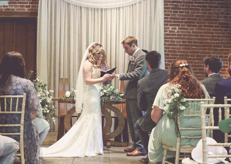 A bride putting the grooms ring on during a wedding ceremony on a wedding day at Haughley Park Barn photographed by suffolk wedding photographer Hayley Denston Photography
