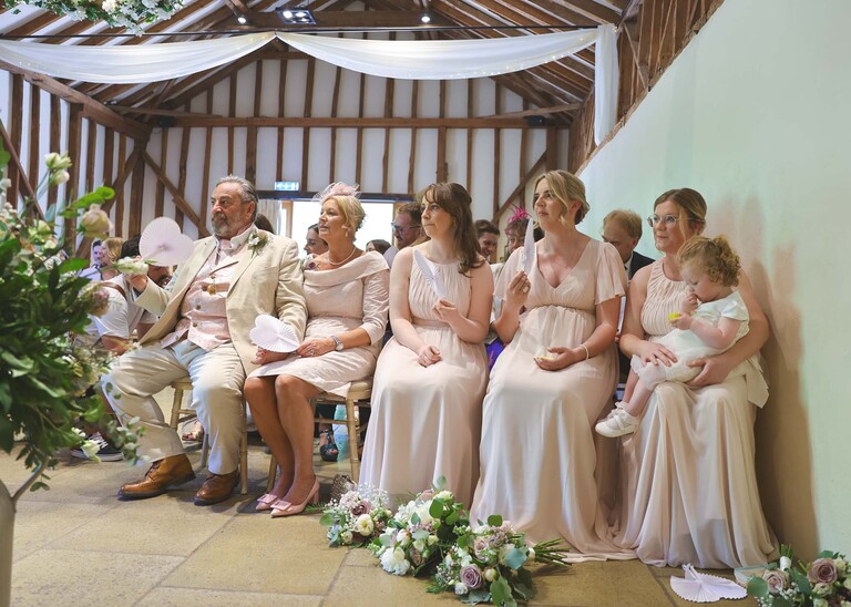 The bridesmaids and parents sat in the front row during a wedding ceremony on a wedding day at Haughley Park Barn photographed by suffolk wedding photographer Hayley Denston Photography