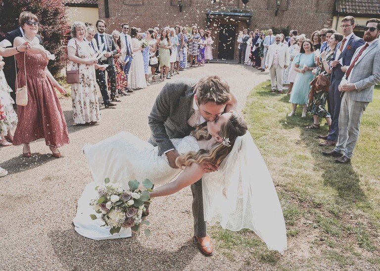 A bride being dipped by her groom at the end of a confetti aisle and kissing on a wedding day at Haughley Park Barn photographed by suffolk wedding photographer Hayley Denston Photography