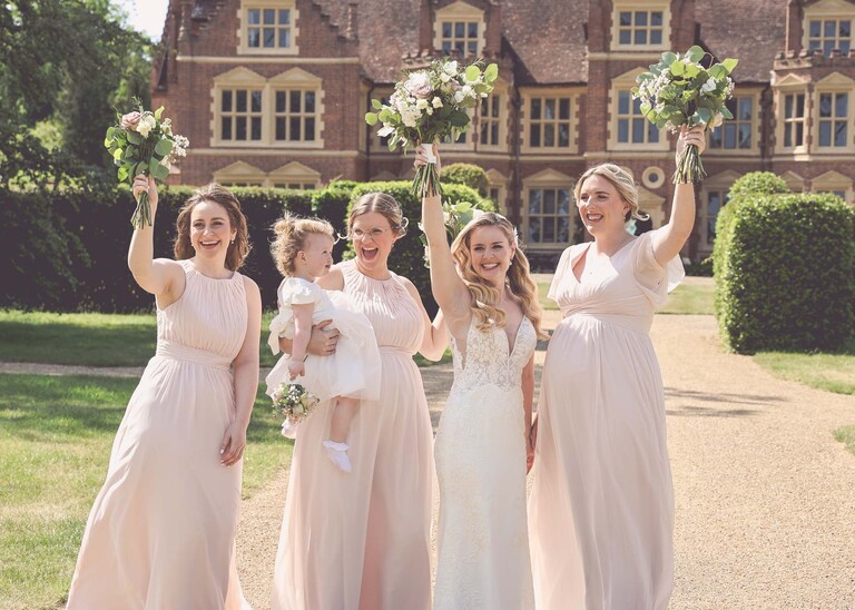 A bride and bridesmaids with their bouquets in the air on a wedding day at Haughley Park Barn photographed by suffolk wedding photographer Hayley Denston Photography