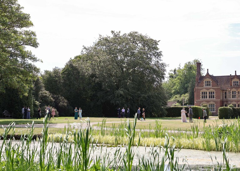 Guests mingling and enjoying garden games with a pond in front of them on a wedding day at Haughley Park Barn photographed by suffolk wedding photographer Hayley Denston Photography