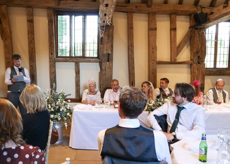 A bestman giving his speech beside the top table on a wedding day at Haughley Park Barn photographed by suffolk wedding photographer Hayley Denston Photography
