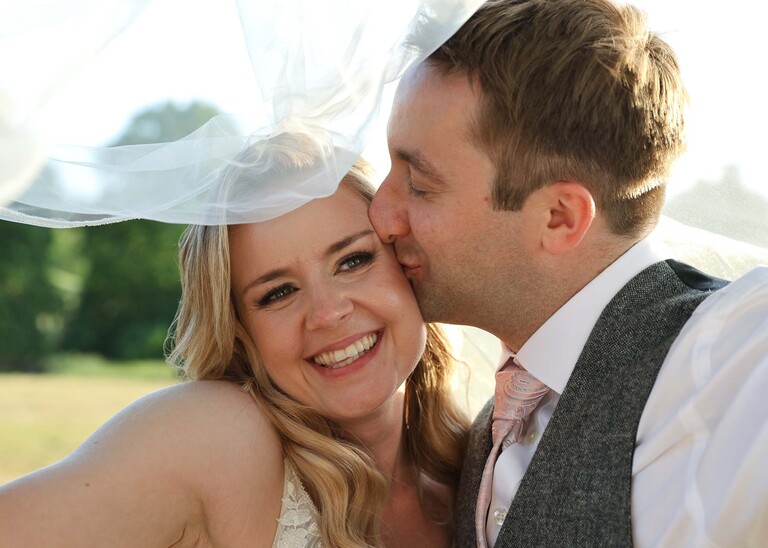 A groom kissing his bride under her veil during golden hour on a wedding day at Haughley Park Barn photographed by suffolk wedding photographer Hayley Denston Photography