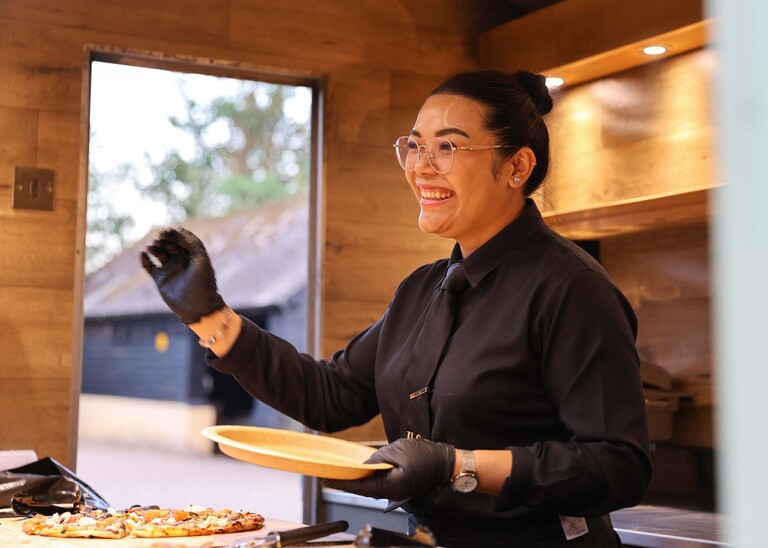 A waitress smiling and serving pizza at a wedding reception on a wedding day at Haughley Park Barn photographed by suffolk wedding photographer Hayley Denston Photography