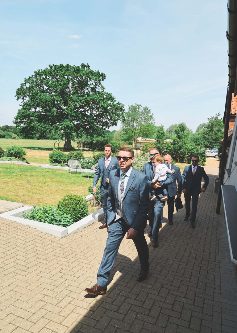 Groomsmen in blue suits walking to the wedding venue on a wedding day at Little Green Wedding Barn photographed by suffolk wedding photographer Hayley Denston Photography