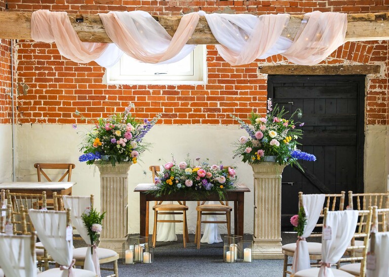 A ceremony room with flowers on pedestals and the top table on a wedding day at Little Green Wedding Barn photographed by suffolk wedding photographer Hayley Denston Photography