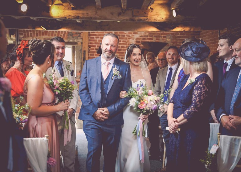 A bride and her dad walking up the aisle in the ceremony room on a wedding day at Little Green Wedding Barn photographed by suffolk wedding photographer Hayley Denston Photography