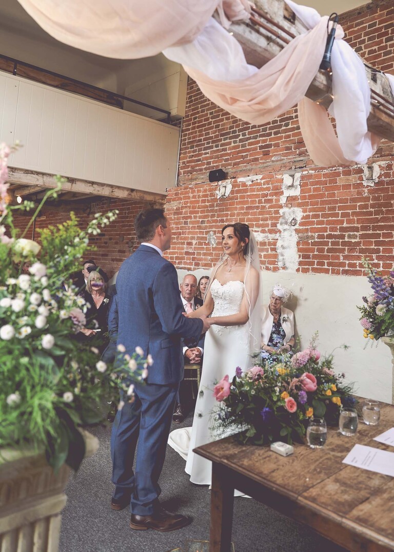 A bride and groom exchanging wedding vows and holding hands during a wedding ceremony on a wedding day at Little Green Wedding Barn photographed by suffolk wedding photographer Hayley Denston Photography