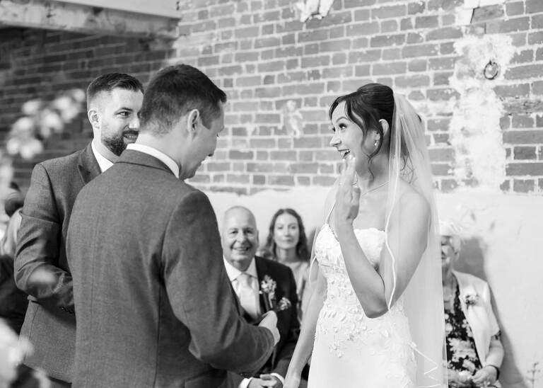 A black and white photo of the bride holding up her hand with a ring on her finger to show the guests on a wedding day at Little Green Wedding Barn photographed by suffolk wedding photographer Hayley Denston Photography