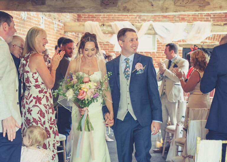 A bride and groom walking back down the aisle newly married on a wedding day at Little Green Wedding Barn photographed by suffolk wedding photographer Hayley Denston Photography