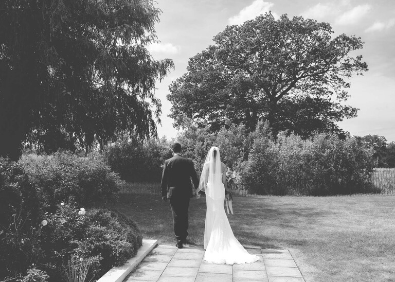 A black and white photo of the bride and groom walking away after getting married on a wedding day at Little Green Wedding Barn photographed by suffolk wedding photographer Hayley Denston Photography