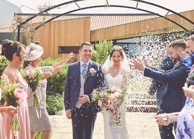 A bride and groom walking through a confetti aisle on a wedding day at Little Green Wedding Barn photographed by suffolk wedding photographer Hayley Denston Photography