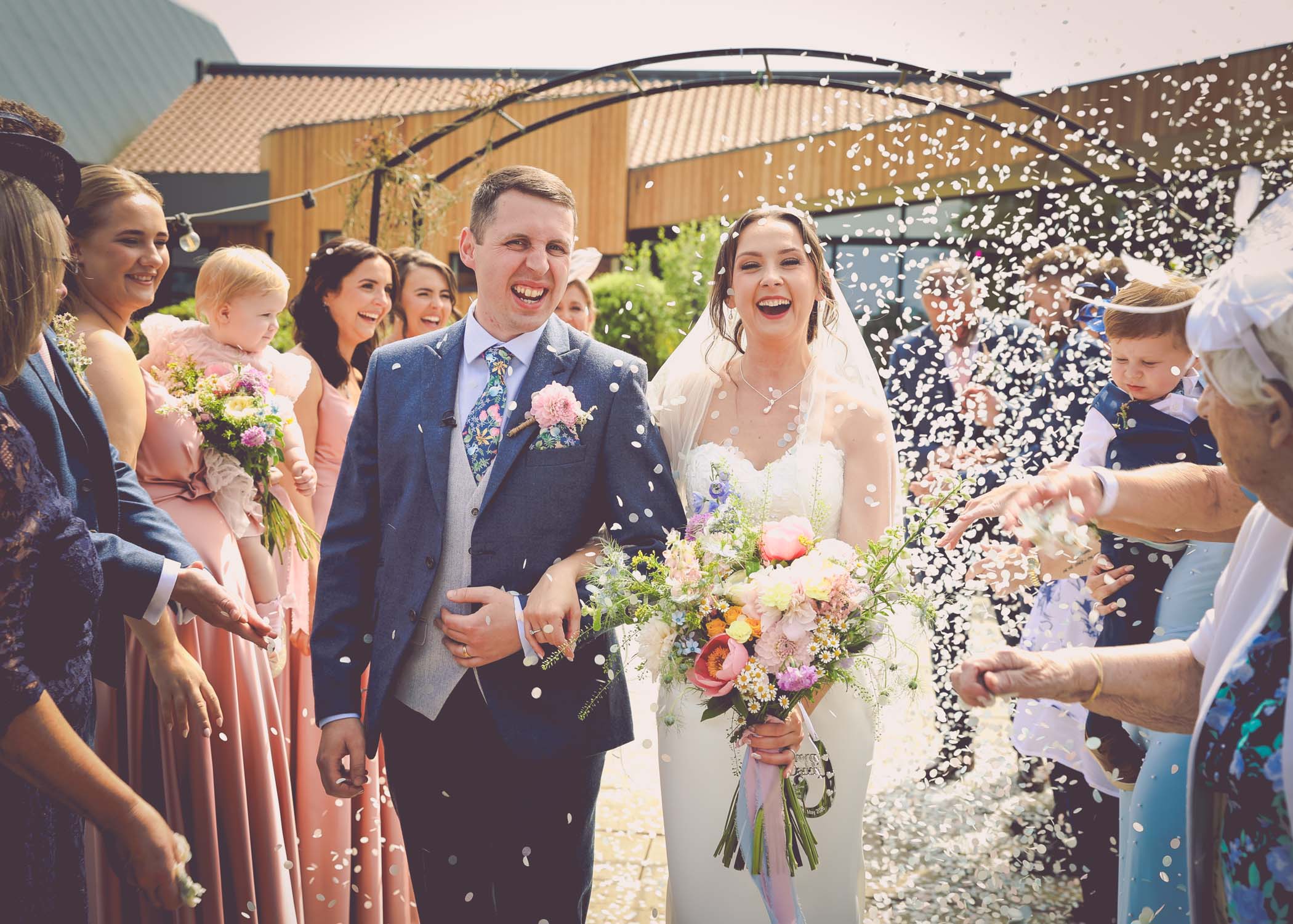 A bride and groom walking through a confetti aisle on a wedding day at Little Green Wedding Barn photographed by suffolk wedding photographer Hayley Denston Photography