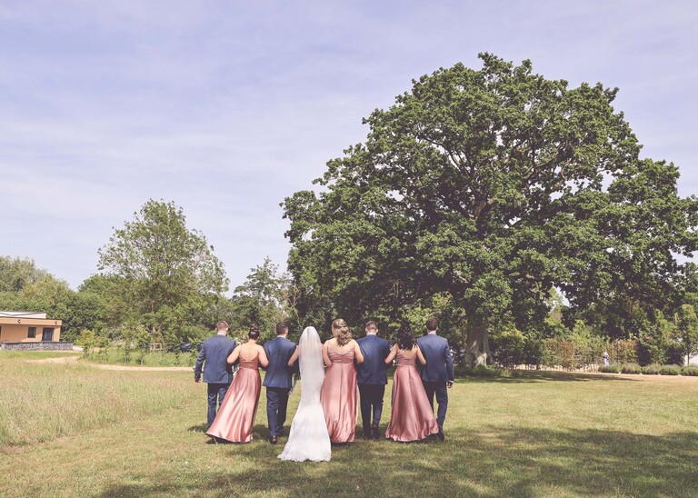 A bridal party walking towards an oak tree on a wedding day at Little Green Wedding Barn photographed by suffolk wedding photographer Hayley Denston Photography
