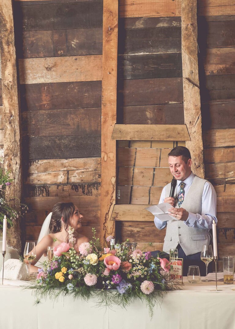 A groom looking at his bride and son during the wedding speeches on a wedding day at Little Green Wedding Barn photographed by suffolk wedding photographer Hayley Denston Photography