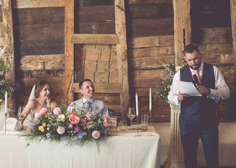 A bestman giving his speech whilst the bride and groom listen on a wedding day at Little Green Wedding Barn photographed by suffolk wedding photographer Hayley Denston Photography