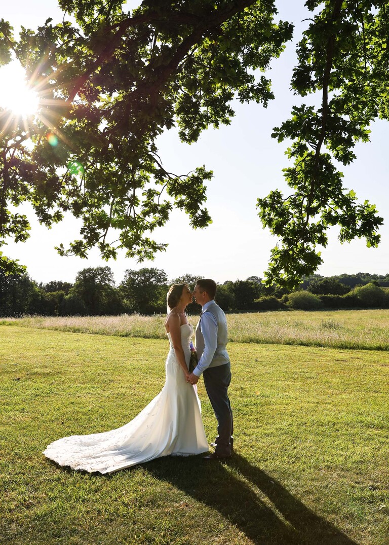 A bride and groom kissing at golden hour underneath an oak tree on a wedding day at Little Green Wedding Barn photographed by suffolk wedding photographer Hayley Denston Photography