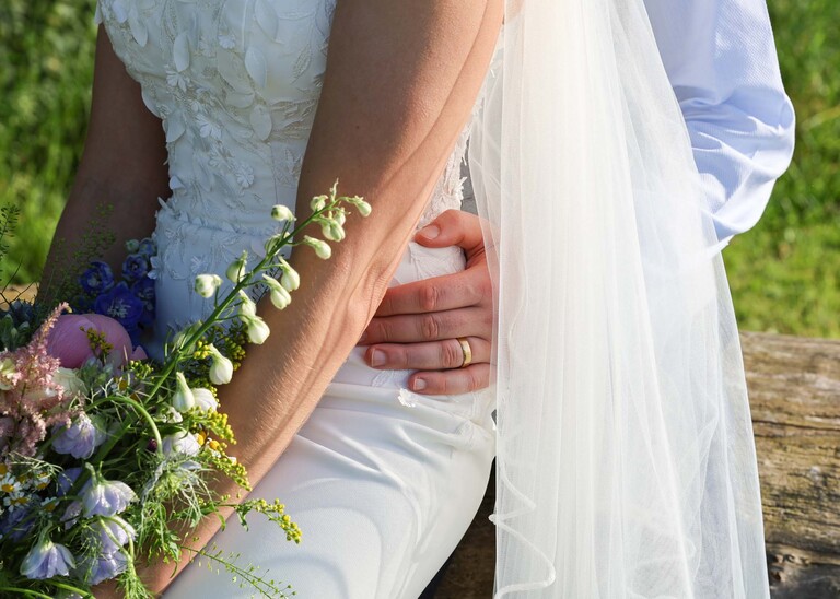 A grooms hand with his wedding ring held around the brides waist on a wedding day at Little Green Wedding Barn photographed by suffolk wedding photographer Hayley Denston Photography